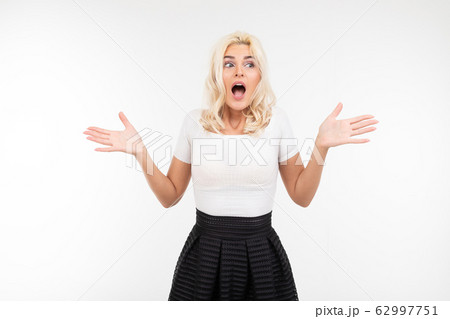 portrait of a surprised blond girl in a white T-shirt waving her arms to the sides on a white portrait of a surprised blond girl in a white T-shirt waving her arms to the sides on a white 62997751