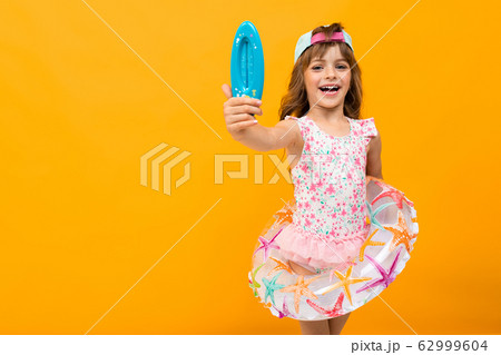 Beautiful little girl in swinsuit holds a rubber ring and shows a thermometer for a water isolated 62999604