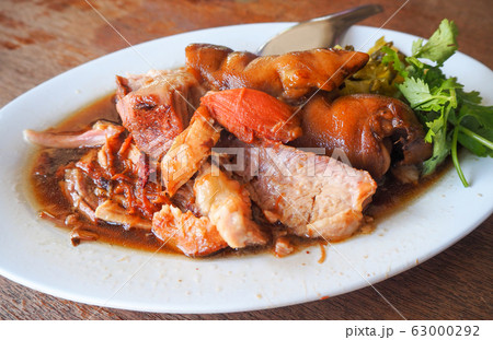 Thai food, stewed pork leg in a white oval plate There are some pieces, cut in half, topped with water. Some of the pieces are the nails of the pig called kaki, parsley decorated on the side. 63000292