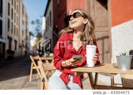 Woman with phone and coffee on the cafe terrace outdoors 63004675