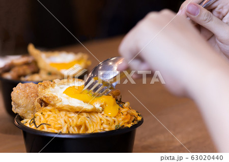 Hand holding spoon and fork cutting egg with noodle soup on wooden table. Hand holding spoon and fork cutting egg with noodle soup on wooden table. 63020440