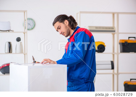 Young male contractor repairing refrigerator at workshop Young male contractor repairing refrigerator at workshop 63028729