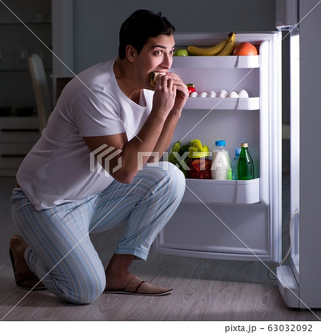 Man at the fridge eating at night 63032092