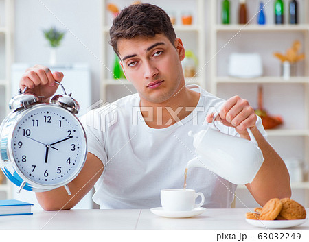 Man with alarm clock falling asleep at breakfast Man with alarm clock falling asleep at breakfast 63032249