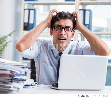 Young businessman under pressure in office to deliver tasks Young businessman under pressure in office to deliver tasks 63032308