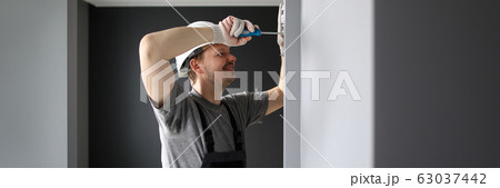 Young smiling repairman standing in empty flat and fixing electricity with screwdriver Young smiling repairman standing in empty flat and fixing electricity with screwdriver 63037442