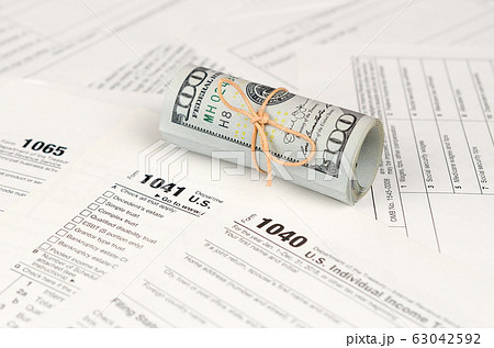 Tax forms lies near roll of hundred dollar bills. Tax forms lies near roll of hundred dollar bills. 63042592
