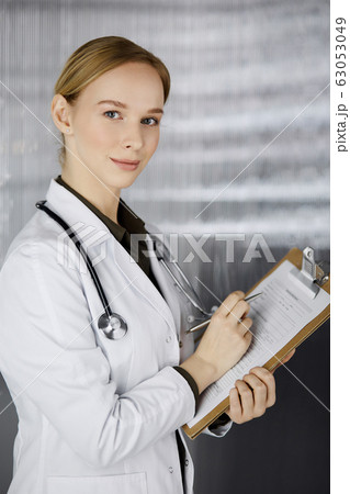 Cheerful smiling female doctor using clipboard in clinic. Portrait of friendly physician woman at work. Perfect medical service in hospital. Medicine concept 63053049