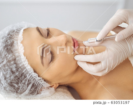 Beautician doing beauty procedure with syringe to face of young brunette woman. Cosmetic medicine and surgery, beauty injections 63053197