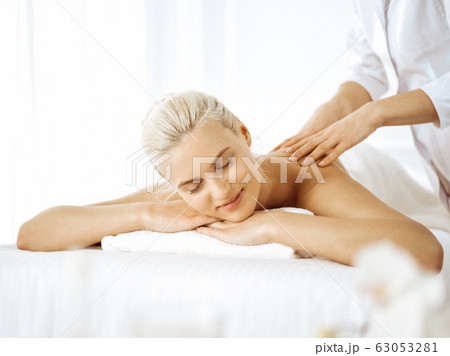 Beautiful blonde woman enjoying back massage with closed eyes. Spa salon concept Beautiful blonde woman enjoying back massage with closed eyes. Spa salon concept 63053281