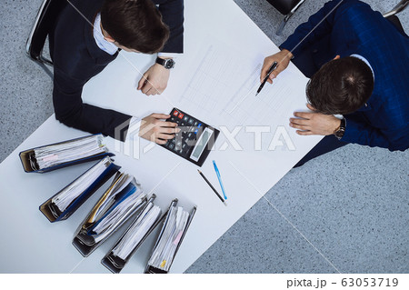 Business people at meeting, view from above. Bookkeeper or financial inspector making report, calculating or checking balance Business people at meeting, view from above. Bookkeeper or financial inspector making report, calculating or checking balance 63053719