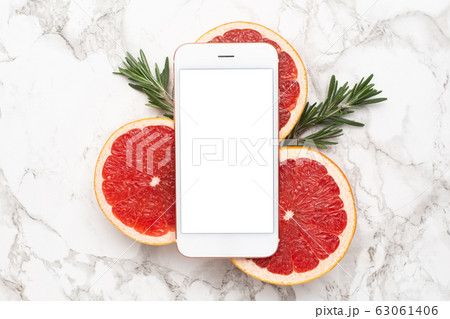 Mobile phone and grapefruits with rosemary on marble background, fruit and technology flatlay, summer minimal compositon Mobile phone and grapefruits with rosemary on marble background, fruit and technology flatlay, summer minimal compositon 63061406
