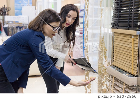 Female salesman and buyer in the fabric store are looking to select samples of materials Female salesman and buyer in the fabric store are looking to select samples of materials 63072866