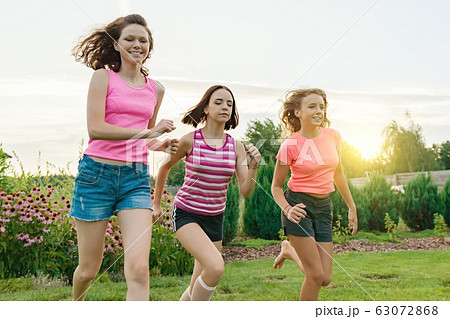 Three young sports girls teenagers running on a green lawn against the backdrop of summer sunset 63072868