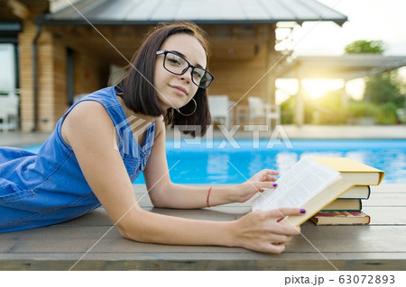 Cute student girl reading book lying near the pool. Education, summer, knowledge Cute student girl reading book lying near the pool. Education, summer, knowledge 63072893