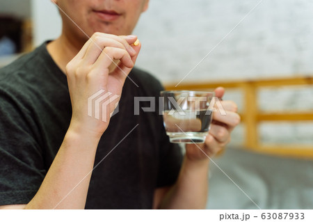 Young Asian man feeling sick and taking pills while sitting on the bed at home 63087933
