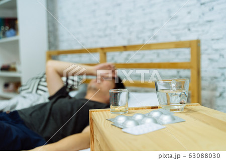 Young Asian man feeling sick and ill lying on bed with medicines tablets and pills on table Young Asian man feeling sick and ill lying on bed with medicines tablets and pills on table 63088030