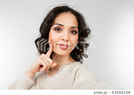 pretty brunette with makeup girl taking selfie while grimacing on gray studio background pretty brunette with makeup girl taking selfie while grimacing on gray studio background 63088106