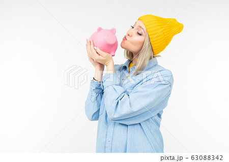 stylish girl in a blue shirt with a bank for saving finances on a white background with copy space stylish girl in a blue shirt with a bank for saving finances on a white background with copy space 63088342