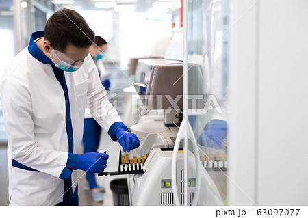 Male researcher checking test tubes while using research machine Male researcher checking test tubes while using research machine 63097077