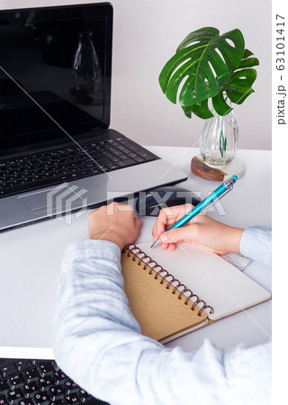 Workplace with laptop, boy puple's hands with pan above notebook and green plant on a white table. Workplace with laptop, boy puple's hands with pan above notebook and green plant on a white table. 63101417