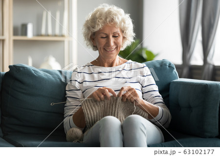Happy 60s grandmother relax on couch doing knitting Happy 60s grandmother relax on couch doing knitting 63102177