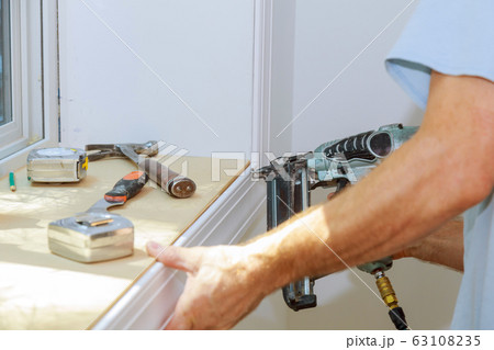 Carpenter using air nail gun to moldings for 63108235