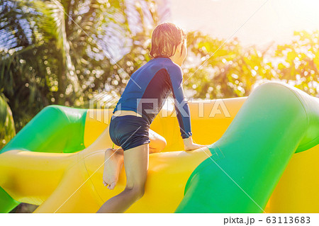 Cute boy runs an inflatable obstacle course in the pool 63113683