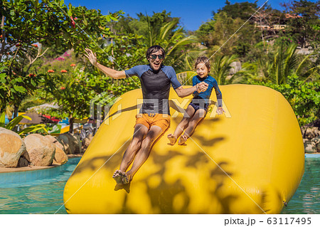 Dad and son go through an inflatable obstacle course in the pool Dad and son go through an inflatable obstacle course in the pool 63117495