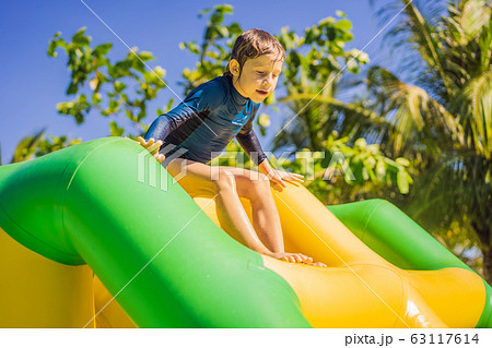 Cute boy runs an inflatable obstacle course in the pool Cute boy runs an inflatable obstacle course in the pool 63117614