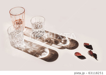 Summer still life scene. Glittering glasses of water or cocktails and cut figs fruit on pink table background in sunlight. Long harsh shadows. High angle. Refreshment, vacation concept. 63118251