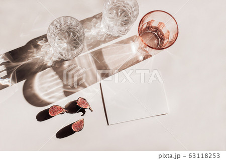 Summer stationery still life scene. Glasses of water, cut figs fruit. Pink table background in sunlight. Blank business, greeting card, invitation mockup scene. Long harsh shadows. Flat lay, top view 63118253