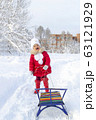 Winter fun. Beautiful little girl in a red coat and mittens smiles and holds a sled on a rope. Snow covered path, trees and snowdrifts. Frosty snowy weather. Clear winter day. Wonderful holidays 63121929