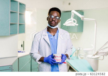 Black dentist in a dental clinic holds artificial jaws in his arms 63124582