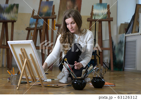 Woman artist sits on the floor among easels with 63126312