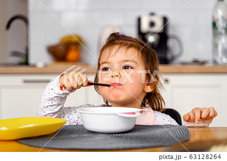 Baby toddler girl eats soup with spoon in her hand.  63128264