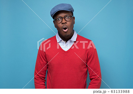 Black african american man in red sweater and blue hat looking surprised. Black african american man in red sweater and blue hat looking surprised. 63133988