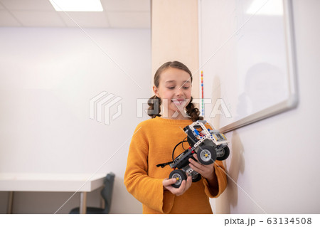 Girl standing at whiteboard, holding buildable car, looking at it Girl standing at whiteboard, holding buildable car, looking at it 63134508