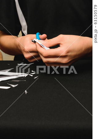 The boy folds and cuts white paper with his hands The boy folds and cuts white paper with his hands 63150579