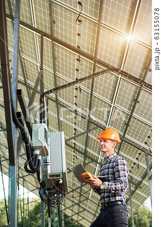 Checking the operation of solar power plant. Man in helmet and with laptop at station 63155078