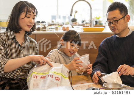 非常持ち出し袋に荷物を入れる子どもを見守る夫婦 63161493