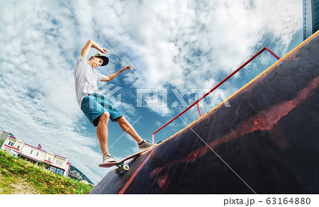 Portrait of a young skateboarder doing a trick on his skateboard on a halfpipe ramp in a skate park in the summer on a sunny day. The concept of youth culture of leisure and sports Portrait of a young skateboarder doing a trick on his skateboard on a halfpipe ramp in a skate park in the summer on a sunny day. The concept of youth culture of leisure and sports 63164880
