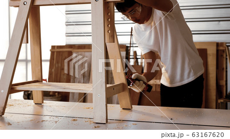Carpenter using drill to screwing pieces of board at site. 63167620