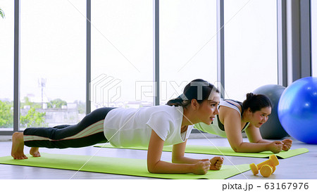 Young shapely woman and chubby woman doing exercise by planking together in the fitness room. Young shapely woman and chubby woman doing exercise by planking together in the fitness room. 63167976