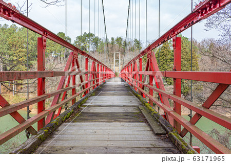 Winter view of red wooden suspension footbridge over lake in forest valley in countryside. Ishikawaken Forest Park, Kanazawa, Japan. Winter view of red wooden suspension footbridge over lake in forest valley in countryside. Ishikawaken Forest Park, Kanazawa, Japan. 63171965