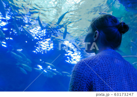 Woman looking at fish vortex in large public aquarium tank at oceanarium Woman looking at fish vortex in large public aquarium tank at oceanarium 63173247
