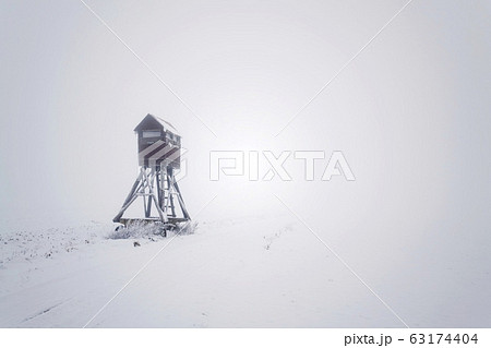 Deer stand, wooden hunters high seat hide on snow covered field, winter foggy day 63174404