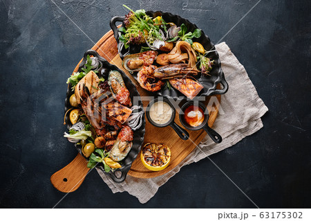 grilled seafood platter. Assorted delicious grilled seafood with vegetables. Grilled mixed bastards with pepper sauce and vegetables. Blue background grilled seafood platter. Assorted delicious grilled seafood with vegetables. Grilled mixed bastards with pepper sauce and vegetables. Blue background 63175302