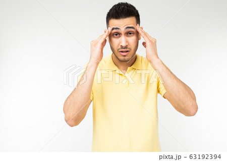brunette man feels a severe headache and holds his head in his hands on a white studio background 63192394
