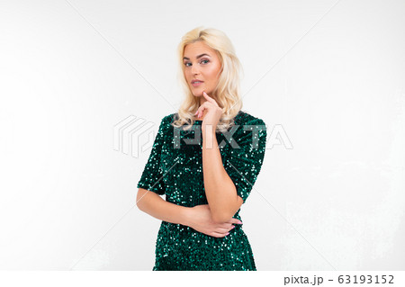 girl in elegant green shiny dress makes a pensive look on a white studio background girl in elegant green shiny dress makes a pensive look on a white studio background 63193152
